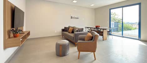 A modern living room with a sofa, ottoman, and a dining area with a table and chairs.