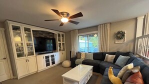 A living room with a dark-colored sofa, a white coffee table, and a television on a cabinet. - Ward Lake Retreat - Lake View, Neighborhood Dock & Sports Court (Olympia)