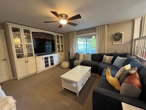 A living room with a dark-colored sofa, a white coffee table, and a television on a cabinet. - Ward Lake Retreat - Lake View, Neighborhood Dock & Sports Court (Olympia)