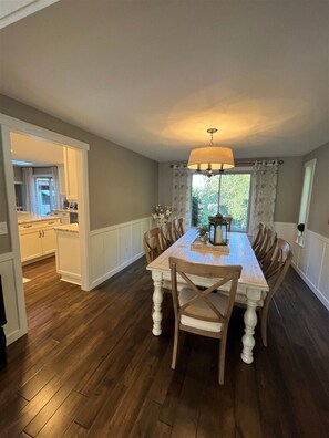 A dining area with a wooden table and chairs, a chandelier, and a view of the kitchen. - Ward Lake Retreat - Lake View, Neighborhood Dock & Sports Court (Olympia)