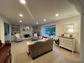 A living room with a beige sofa, a white armchair, a wooden bench, a white dresser, and a fireplace. - Ward Lake Retreat - Lake View, Neighborhood Dock & Sports Court (Olympia)