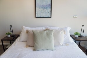 A neatly made bed with white linens, two bedside tables with lamps, and a wall-mounted painting. - Apartment Nearby Metro with Pool (Ñuñoa)