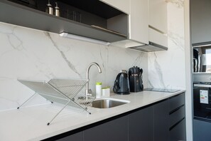 Una cocina moderna con encimera de mármol, pileta de acero inoxidable, un escurreplatos metálico y una cafetera.