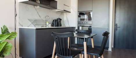 A compact kitchen with a dining area, featuring a modern design with dark cabinetry, a marble backsplash, and a built-in oven.