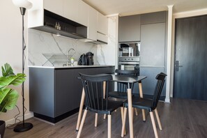 A compact kitchen with a dining area, featuring a modern design with dark cabinetry, a marble backsplash, and a built-in oven. - Apartment Nearby Metro with Pool (Ñuñoa)