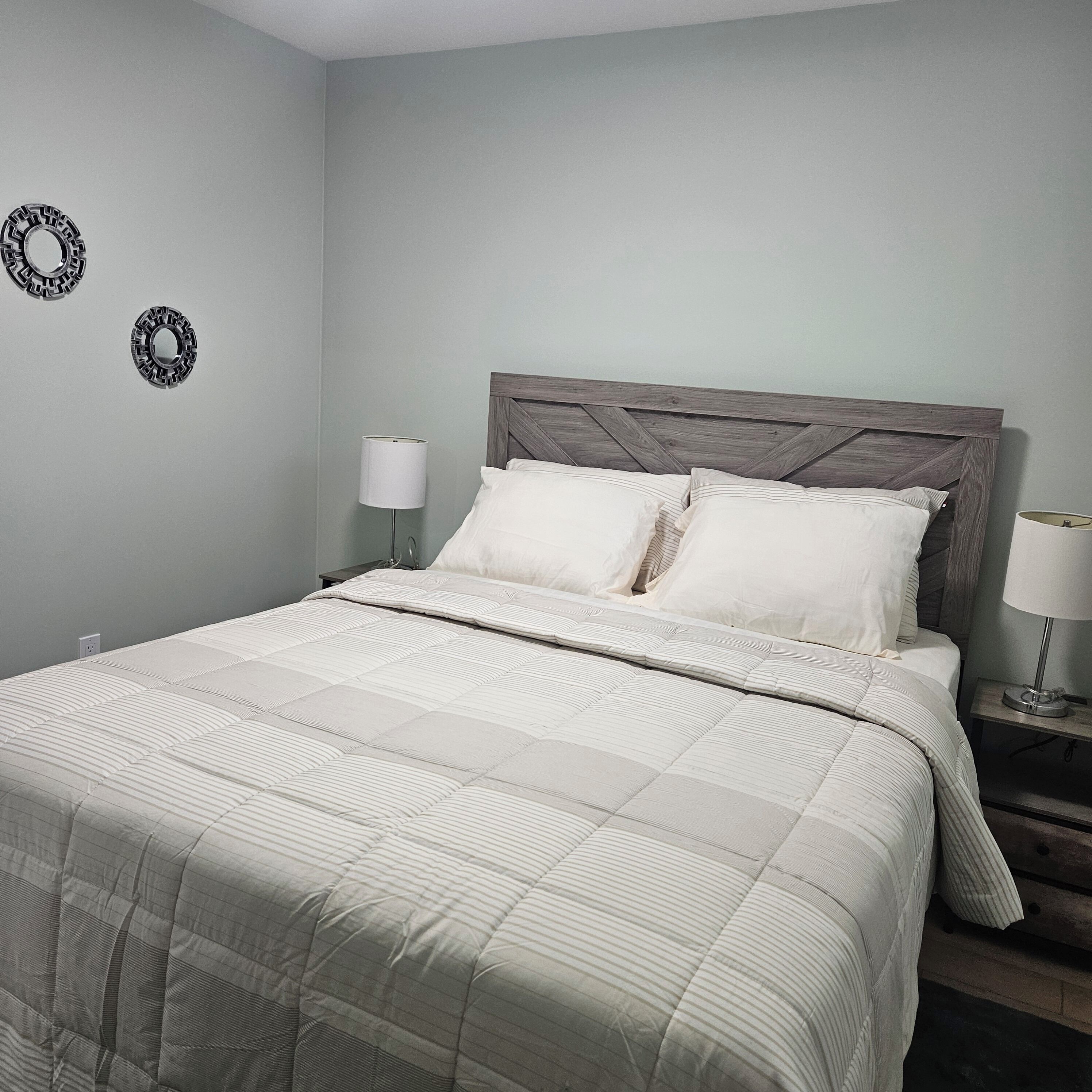 Una cama bien tendida con colcha a rayas y almohadas, un cabecero de madera y dos apliques con lámparas.