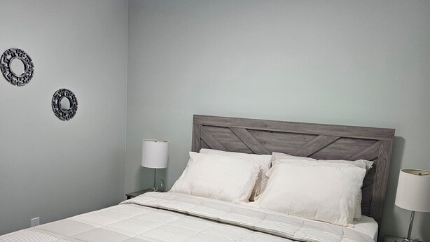 Ein ordentlich bezogenes Bett mit einer gestreiften Tagesdecke und Kissen, ein Holzkopfende und zwei Wandleuchten mit Lampen.