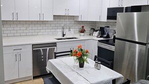 Eine moderne Küche mit weißen Schränken, einem Edelstahl-Kühlschrank, einer Kaffeemaschine und einem Tisch mit Blumen in einer Vase.