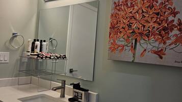 Un baño con lavamanos, espejo, inodoro y un cuadro de flores.