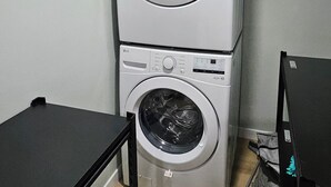 Eine gestapelte Waschmaschine und ein Trockner in einem Waschraum, vor einem schwarzen Tisch.