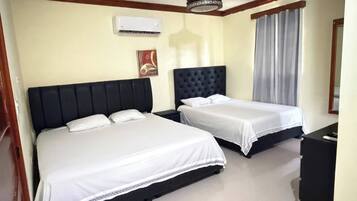 A hotel room with two beds, a ceiling fan, an air conditioning unit, a nightstand, a desk, and a window with curtains.