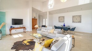 Ein großzügiger Wohnbereich mit Sofa, Couchtisch und Fernseher. Es gibt einen Essbereich mit Stühlen und Tisch.