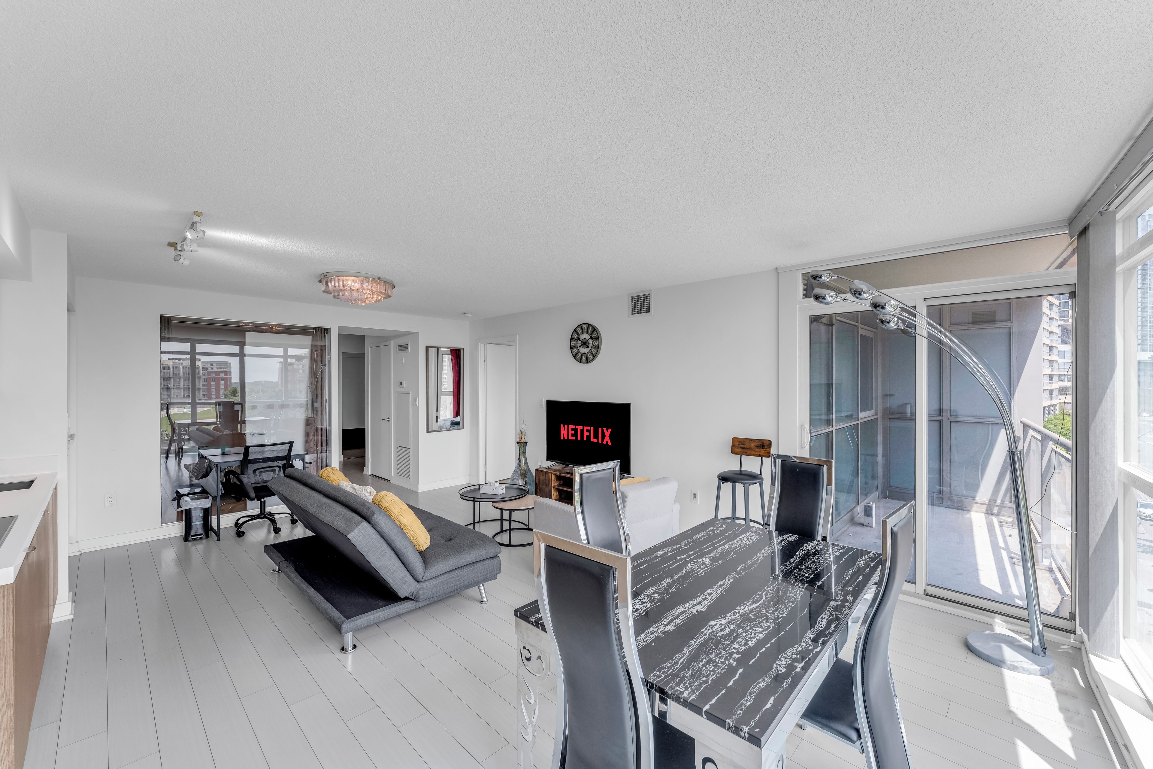 A modern living room with a sofa, a dining table, a TV, and a large window.