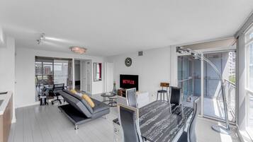 A modern living room with a sofa, a dining table, a TV, and a large window.