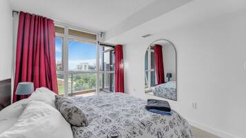 A bedroom with a large bed, a mirror, and a view of buildings through the window.