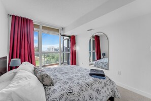 Un dormitorio con una cama grande, un espejo y vistas a edificios a través de la ventana.