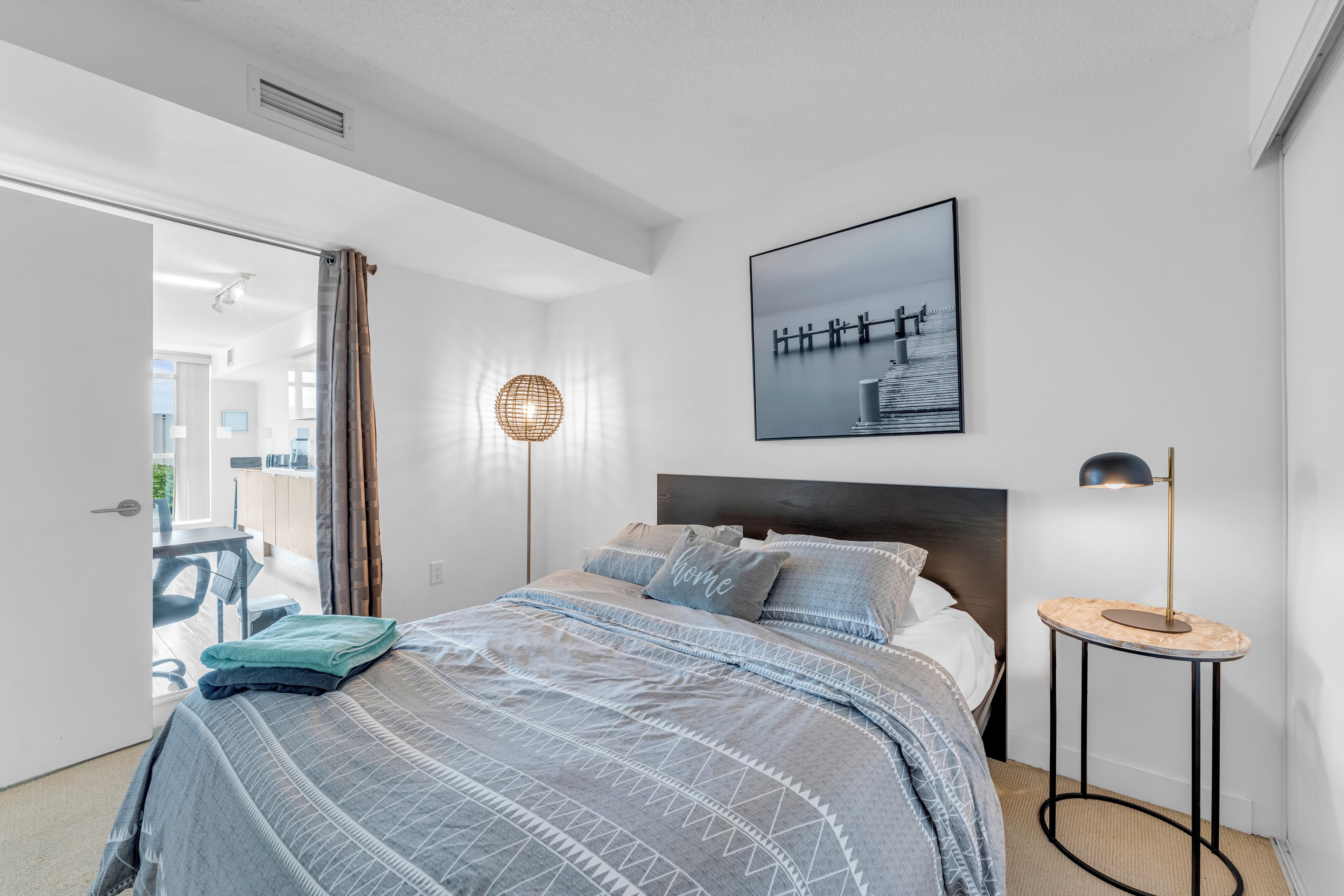 A modern bedroom with a bed, a bedside table, a lamp, and a picture on the wall.