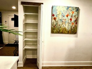 A hallway with a white door leading to a closet with shelves, a painting of flowers on the wall, and a plant in the corner. - House of Gems Relax & Unwind Beautiful Atlanta Home for Families & Groups (Atlanta)
