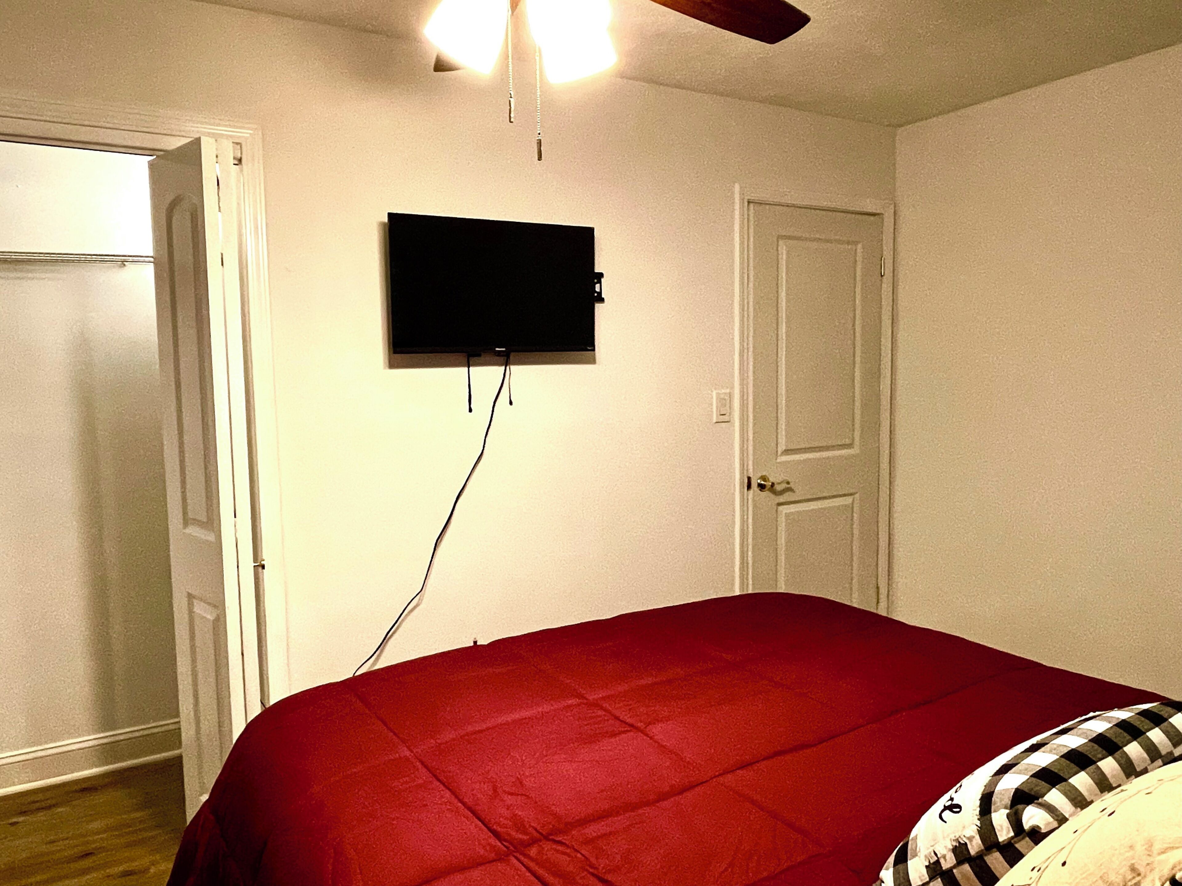 Un dormitorio con cama, televisor en la pared y una puerta.