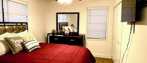 A bedroom with a bed, a dresser, a ceiling fan, a mirror, and a television.
