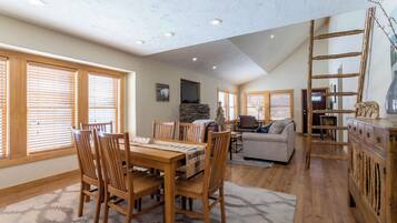 A spacious living area with a dining table, chairs, a fireplace, and a loft space with a ladder.