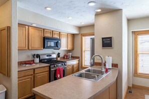 A kitchen with wooden cabinets, a stainless steel sink, a microwave, and a stove.