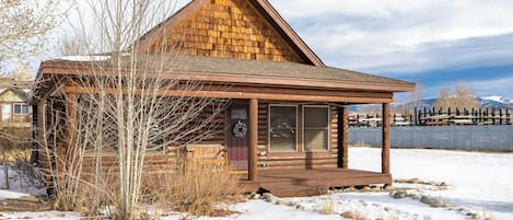 Une cabane en rondins avec une véranda en bois et une cour clôturée.