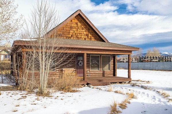 A log cabin with a wooden porch and a fenced yard.