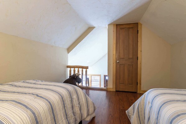 A room with two beds, a wooden door, and a window with blinds.