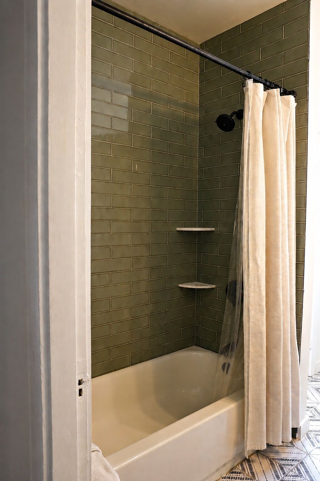 A shower with a glass door, a white bathtub, and a green-tiled wall.