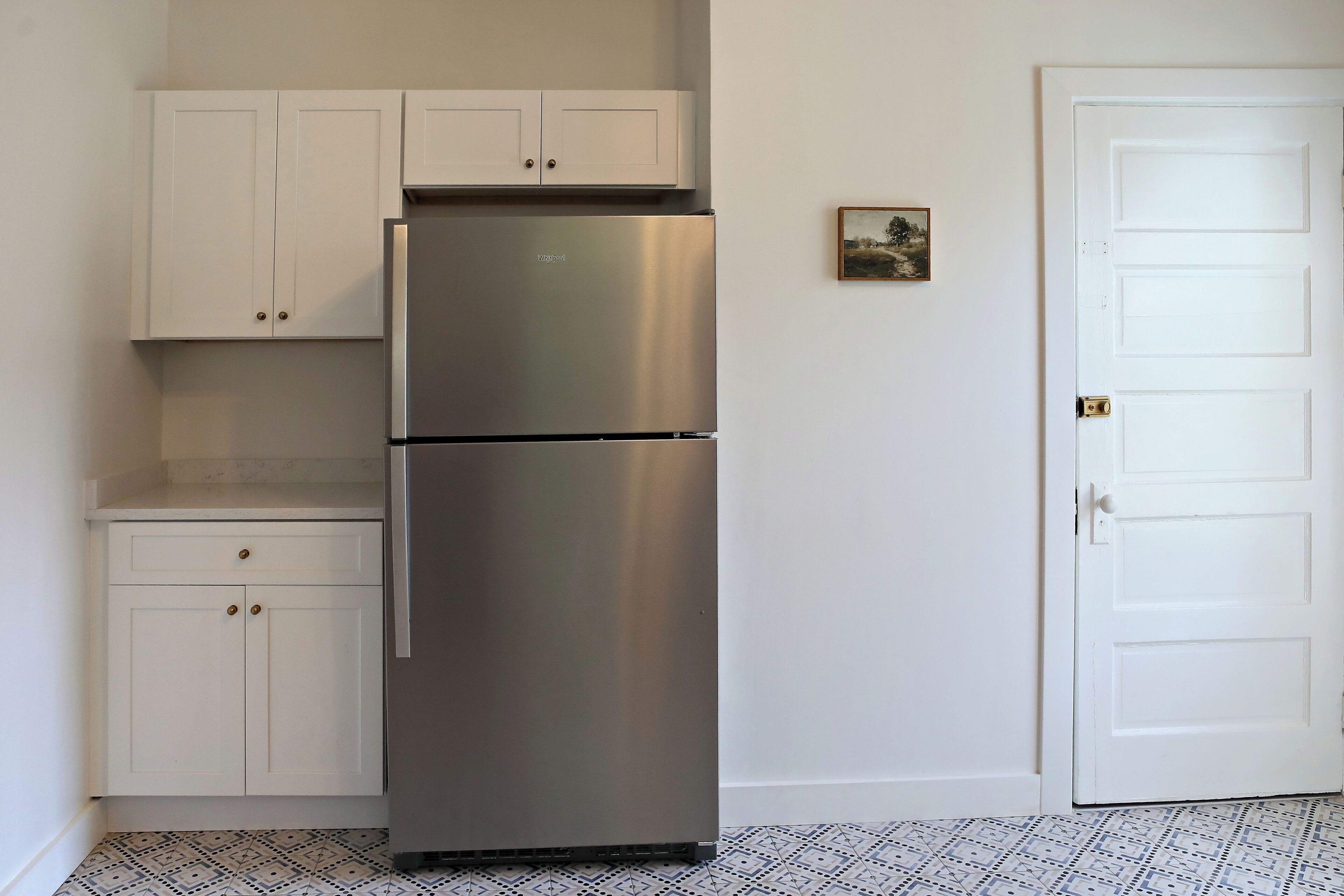 A compact kitchen with a stainless steel refrigerator, white cabinets, and a patterned floor.