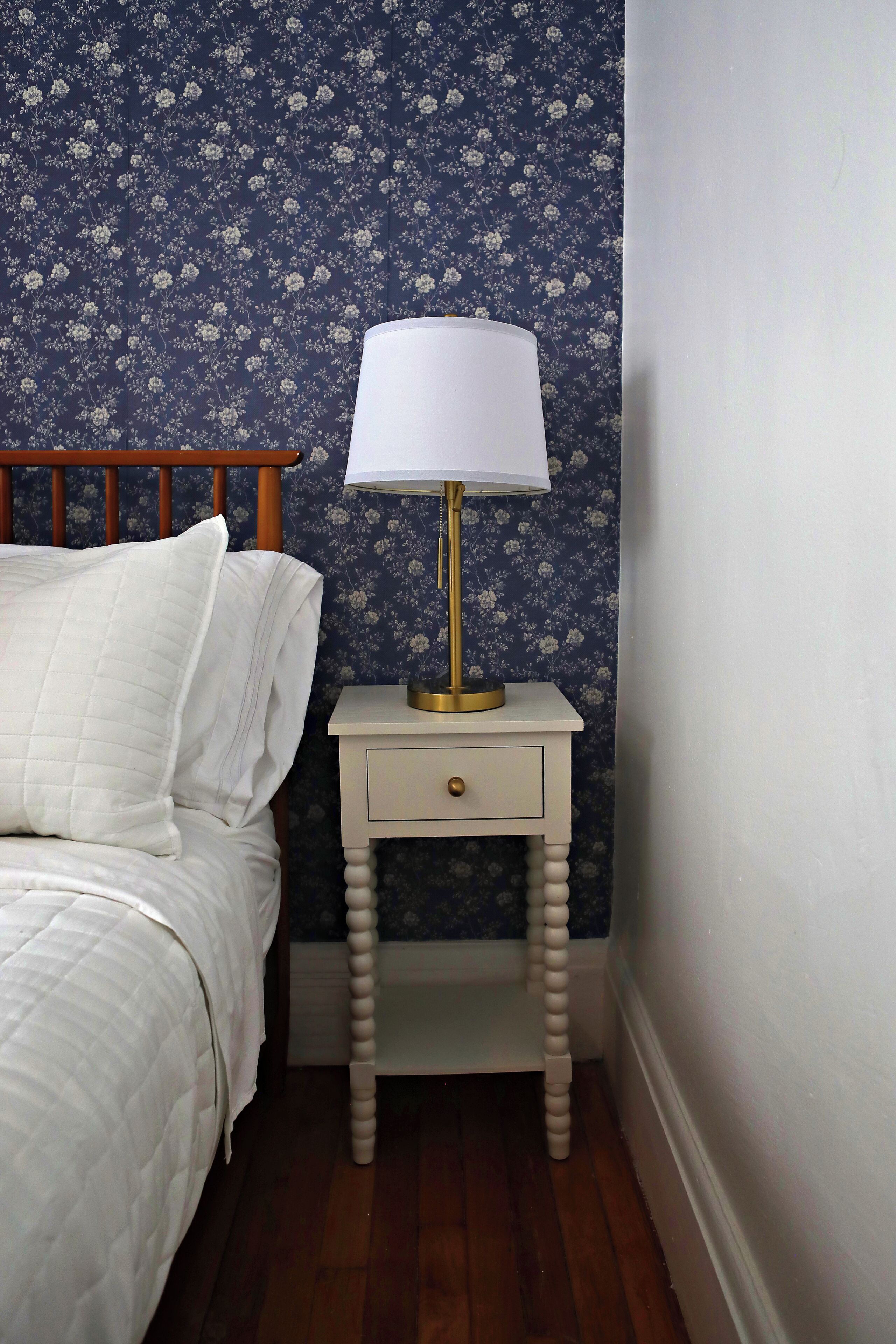 Una camera da letto con un letto, un comodino con una lampada e carta da parati floreale.