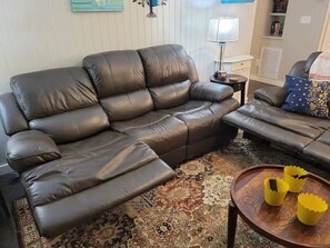 A living room with a brown leather sofa, a patterned rug, and a small wooden table with yellow cups. - Charming cottage in the mountains of NE Georgia, five minutes from Clayton, GA. (Clayton)