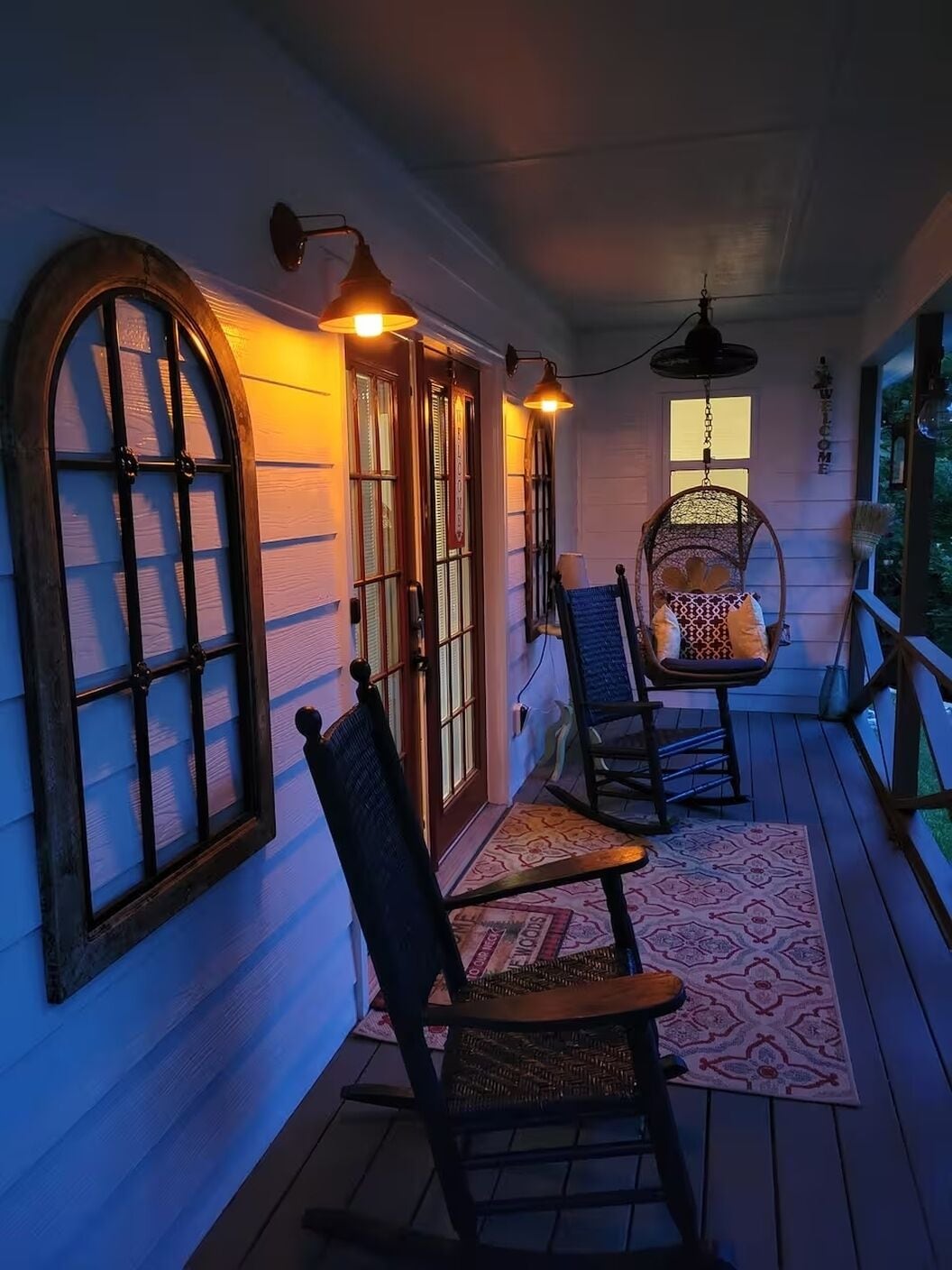 A porch with two rocking chairs, a patterned rug, and a 'WELCOME' sign.