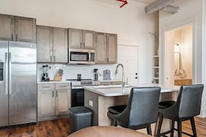A modern kitchen with a stainless steel refrigerator, a microwave, and a stove. There is a small island with a sink and two bar stools.