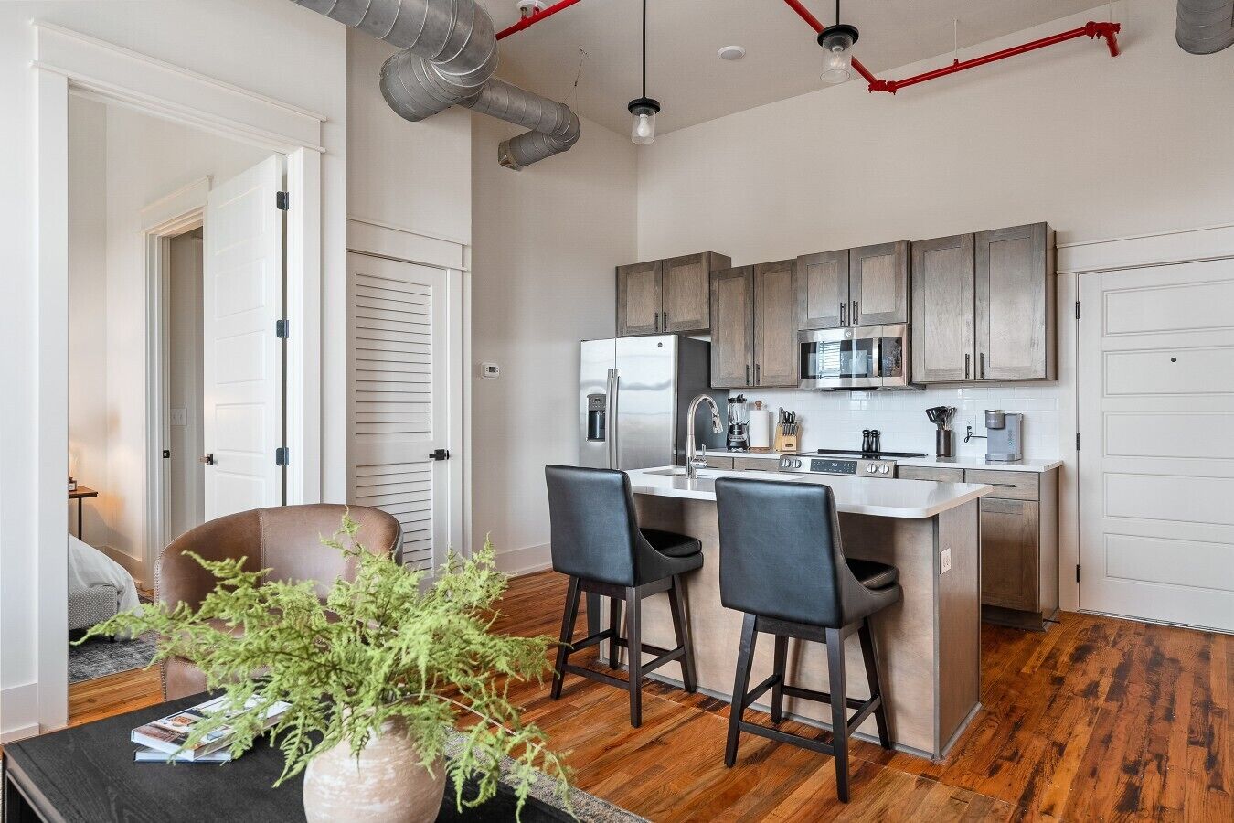 A modern kitchen with stainless steel appliances, a central island with bar stools, and a visible duct system on the ceiling.