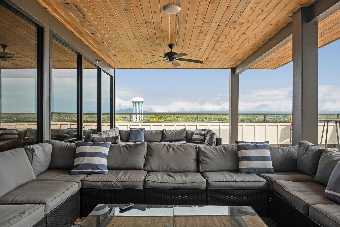 A covered outdoor seating area with a sofa and cushions, large windows, and a ceiling fan.