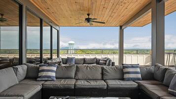 A covered outdoor seating area with a sofa and cushions, large windows, and a ceiling fan.