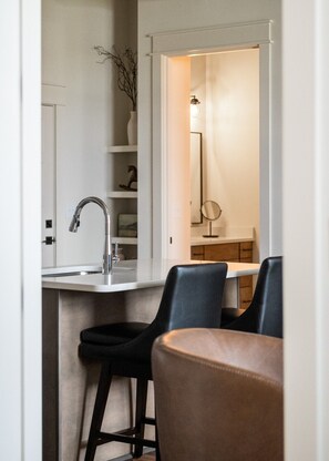 A compact kitchen with a modern faucet, a small countertop, and two bar stools.