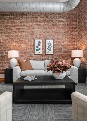 Ein Zimmer mit Backsteinwand, einer Couch, zwei Nachttischen mit Lampen und gerahmten Pflanzenmotiven.
