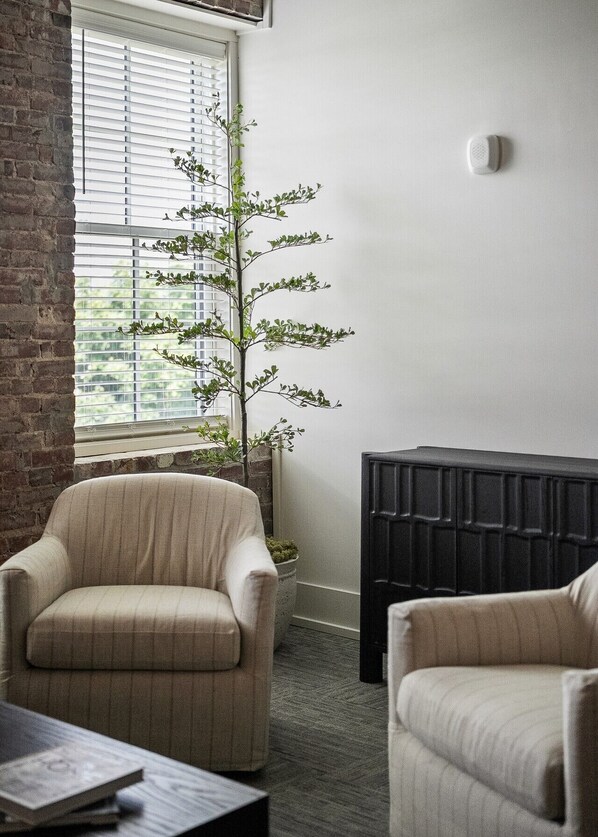 A room with a brick wall, a window with blinds, a potted plant, a fireplace, and two armchairs.