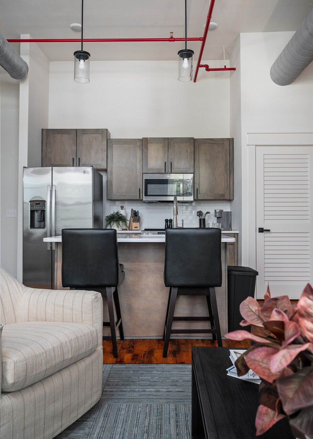 Cocina compacta con electrodomésticos modernos, dos taburetes de bar y una pequeña sala de estar con sofá.