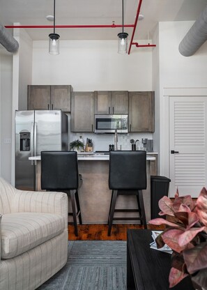 A compact kitchen with modern appliances, two bar stools, and a small seating area with a sofa.