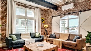 A cozy living room with brick walls, two sofas, a coffee table, and large windows offering a view of the city. - Central City 2bed With Mountain Views Skywood Loft (Cape Town)