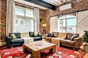 Ein gemütliches Wohnzimmer mit Backsteinwänden, zwei Sofas, einem Couchtisch und großen Fenstern mit Stadtblick.