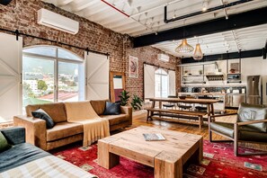 A spacious living area with a large window, a sofa, a coffee table, and a kitchen in the background. - Central City 2bed With Mountain Views Skywood Loft (Cape Town)