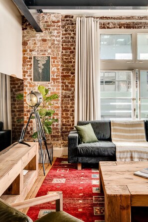 A cozy living room with a brick wall, a black sofa, a wooden coffee table, and a red patterned rug. - Central City 2bed With Mountain Views Skywood Loft (Cape Town)