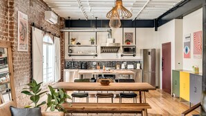 A modern kitchen with a wooden table and bench, a hanging light fixture, and a brick wall. - Central City 2bed With Mountain Views Skywood Loft (Cape Town)
