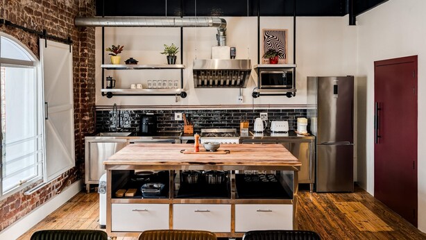 A modern kitchen with a central island, stainless steel appliances, and a brick wall. - Central City 2bed With Mountain Views Skywood Loft (Cape Town)