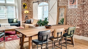 A cozy room with a wooden dining table, four chairs, a sofa, and a lamp. - Central City 2bed With Mountain Views Skywood Loft (Cape Town)